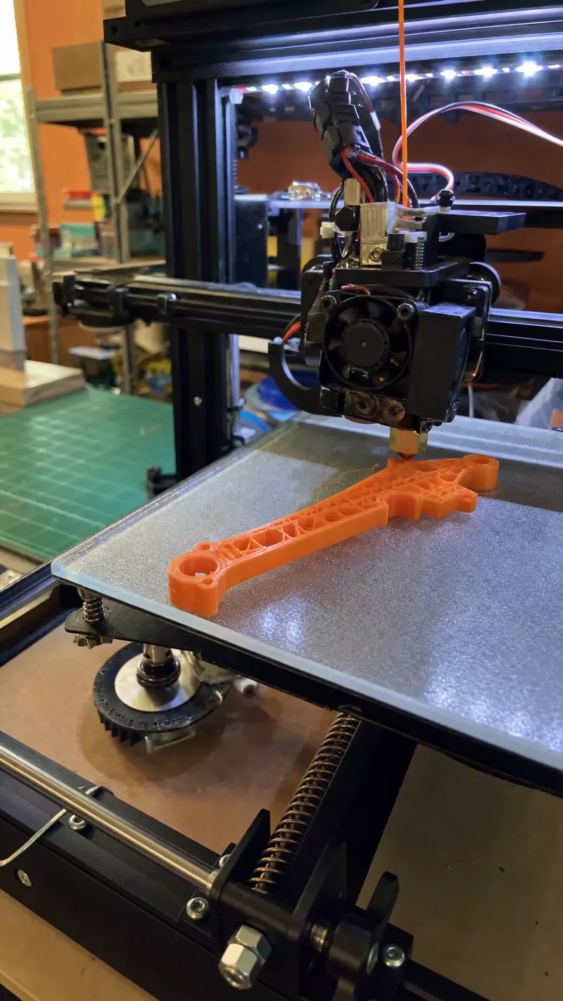 3D yazıcının turuncu filamentle İHA gövde parçası basması, baskı kafası hareket hâlinde